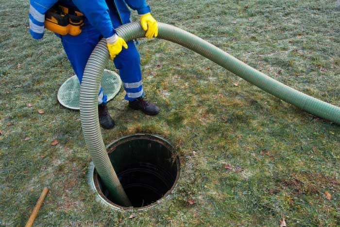 Technician holding a long hose, servicing a septic tank.