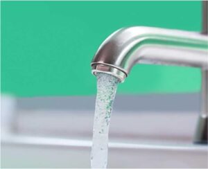Close-up of a stainless steel faucet with water flowing into a sink, against a green background.